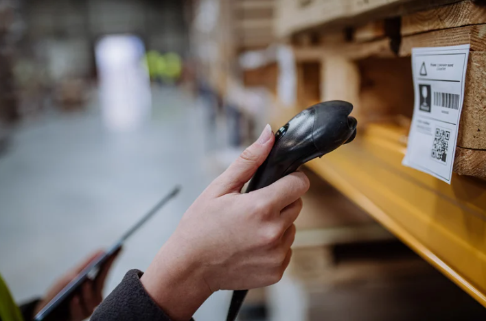Someone scanning a barcode with a scanner gun inside a warehouse.