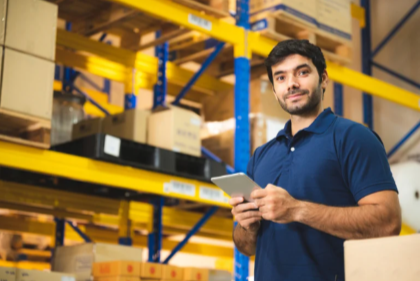 Service-Page-E-commerce-Fulfillment-Hub-Page-Tonal-Rewrite-Google-Docs-07-11-2025_04_28_PM A smiling guy in a blue shirt with a tablet, inside of a 3PL warehouse.